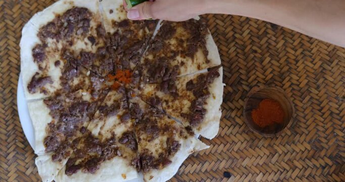 Close up of a hand squeezing lime and putting spices on Manakish Lahm Bi Ajeen - Flatbreads with minced lamb or beef and Fatayer stuffed pie with spinach. Traditional Arab food