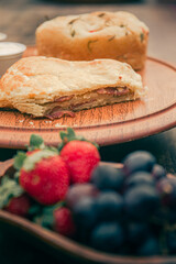 Pastry bread filled with ham at the background and fruits unfocused at the foreground.