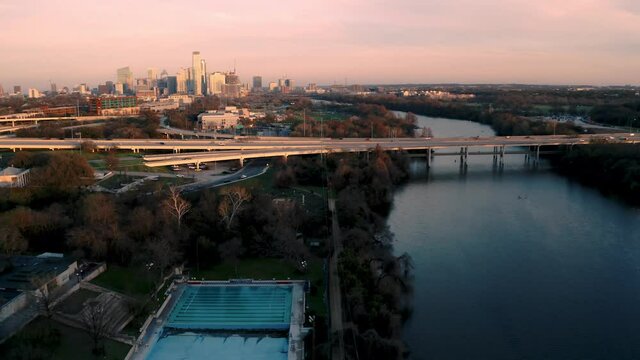 Aerial Drone Flyover Of Deep Eddy Pool With Downtown Austin, Texas Skyline In Background At Sunset