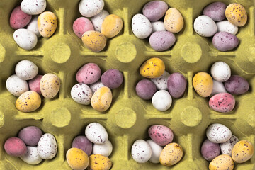 Small mixed colourful eggs in yellow egg tray. Easter background. Top view