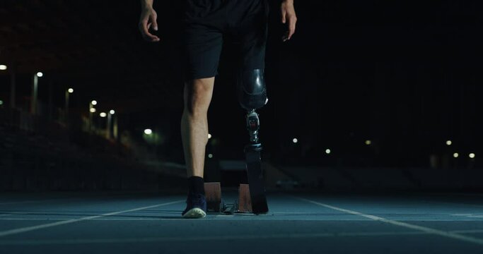 Cinematic close up of disable man with legs prosthesis is warming up before run with dedication on car track at night. Concept of handicapped people active lifestyle, determination, motivation.

