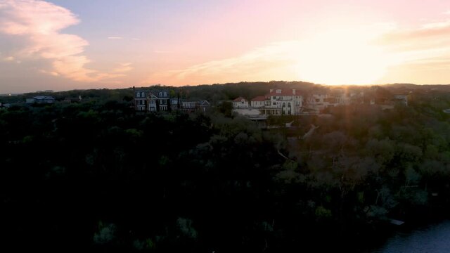 Large homes sit cliffside overlooking water in Downtown Austin, Texas at sunset aerial drone flyover in 4k