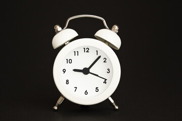white alarm clock with hands on black background