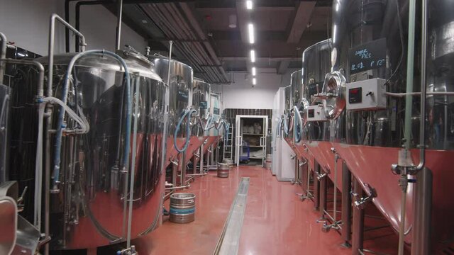 Dollying-in shot overview of empty brewery with huge metal storage tanks and pipes for beer production