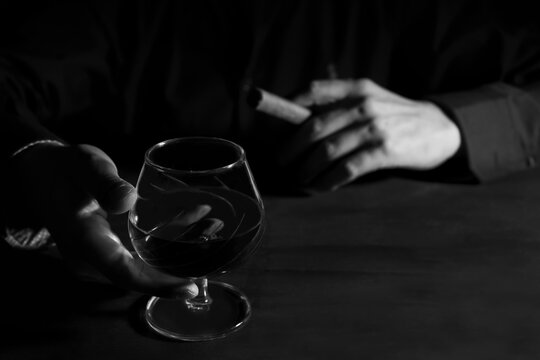 Man hands with a glass of whiskey and a cigar on dark table.Black and white photography,smoke and drink alcohol addiction concept.