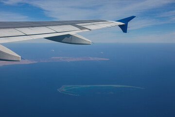 Wing of the airplane and Red sea with islands as seen through the aircraft's porthole