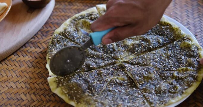 Close up of a hand cutting Zaatar Manakish - Flatbread topped with zaatar and olive oil. Traditional Arab food.