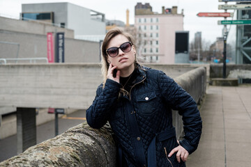 Fototapeta premium Atractive young woman posing near Waterloo bridge in London in a windy and cloudy day. Sunglasses.
