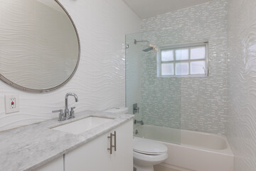 White bathroom with gray marble countertop and round mirror 