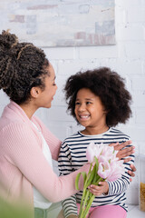 african american woman looking at happy daughter holding fresh tulips