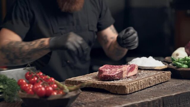 Cook man preparing steak and spinkle salt on the both side of the meat. Slowmotion.