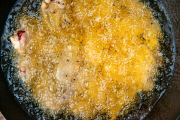chicken frying in high temperature black pan with oil bubble