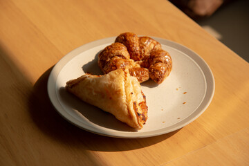 Morning croissant and pie in white plate on wooden table