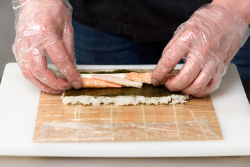Japanese food preparation process close-up. The sushi chef in the restaurant's kitchen prepares a sushi roll with shrimp, cucumber and Philadelphia cheese.