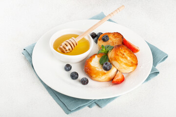 Cottage cheese pancakes, syrniki, with honey and berries in a white plate and black coffee, horizontal view, restaurant serving, breakfast