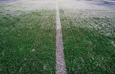 The football field with artificial green grass is covered with a light layer of snow. Early spring. Green grass on the football field is visible from under the snow. Amateur football field.
