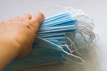 Fototapeta premium A woman's hand holds a stack of disposable medical masks for protection against viral diseases in close-up. Medical surgical blue masks in the hands of a female doctor. Prevention of diseases