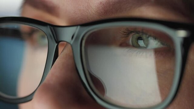 Woman in glasses looking on the monitor and and working with charts and analytics. The monitor screen is reflected in the glasses. Work at night. Extreme close-up