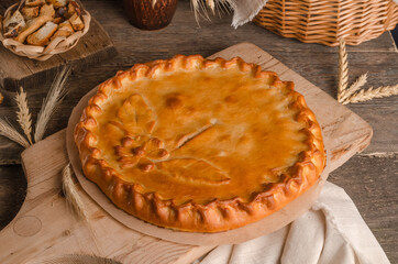 Delicious fresh round pie stuffed with curly dough decorations on wooden