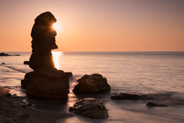 Silhouette of huge rock like idol from Easter Island and rising sun at the seaside. Long exposure