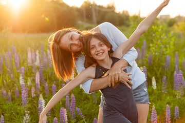 Young mother embracing her child outdoor. Woman and teenage girl on summer field with blooming wild flowers green background. Happy family mom and daughter playing on meadow.