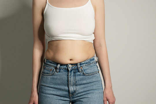 Skinny fat figured unrecognizable woman with belly fat. Woman`s hips closeup raw studio shot in grey background. Dieting and fat loss concept.