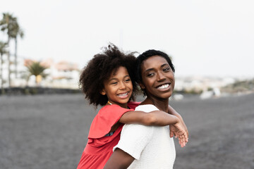 Black mother and daughter walking on the beach at sunset time during summer vacation - Main focus on woman face
