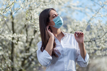 Pretty woman in protective mask near blooming tree