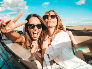 Portrait of two young beautiful and smiling hipster female in convertible car. Sexy carefree women...