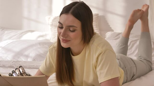 Attractive young woman with metal bionic arm draws in sketchbook lying on bed in contemporary room at home closeup