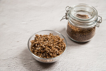 Diet buckwheat porridge in a glass plate and buckwheat groats in a glass jar on a light table.Healthy dietary cereals. Russian cuisine