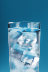 Ice cubes in a glass with crystal clear water on a blue background.