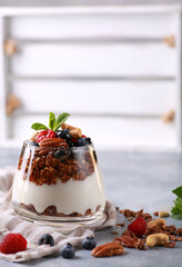 Healthy breakfast. Yogurt,granola, fresh berries with honey in a clear glass. Nuts and fresh mint on a gray light background. Background image, copy space, vertical