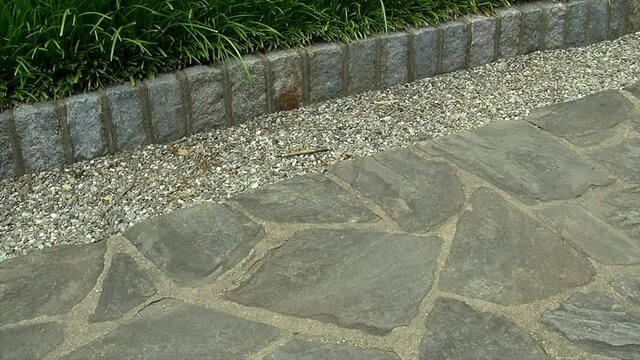 Pan across a flagstone pathway with a border of pebbles and cobblestones.