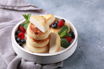 Healthy breakfast. Cheesecakes, cottage cheese pancakes with honey, fresh berries, mint on a white wooden plate on a gray table. Background image, copy space, horizontal