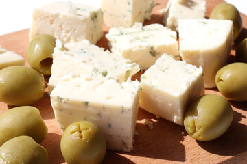 Sliced piece of blue cheese and green olives on wooden board background. Top view, close-up