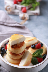 Healthy breakfast. Cheesecakes, cottage cheese pancakes with honey, fresh berries, mint on a white wooden plate on a gray table. Background image, copy space, vertical