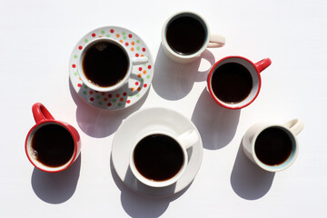 Variety of coffee cups with espresso on white table background. Hard light, shadow. Summer flat lay minimalist composition. Top view, copy space
