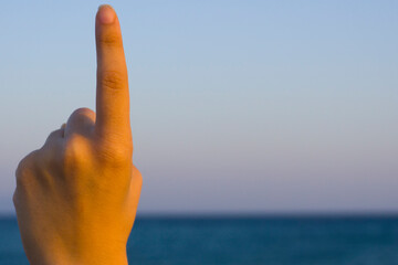 Hand showing number one gesture on blue sea sky background. Gesturing number 1 index finger. Hand pointing upward. Making number one in sign language. Being first. Hand counting one. Space for ad text