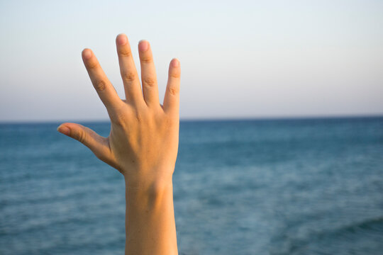 Woman hand doing  showing number five gesture symbol on blue summer sky nature background. Gesturing number 5. Number five in sign language. Fifth, counting down five concept. Five fingers up. 
