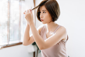 Portrait of beauiful young Asian woman having her hair cut with scissors at home. She's stay at home during the coronavirus pandemic, Self hair care during quarantine.