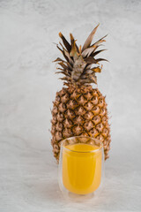 Pineapple fruit and juice in double glass cup on white stone background. Pouring yellow tropical fruit juice into glass.