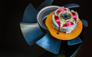 Integrated hall sensor in computer fan rotor and plastic vanes on a black background. Red coils copper wire winding and ball bearing in dismantled EC electric motor with electronic commutation system.