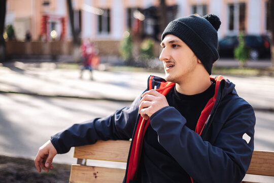 Young adult man outside and smoking tobacco device electronic cigarette heater. Smoke and steam system with sticks inside, image with copy space. Harmful habit harm to health lungs
