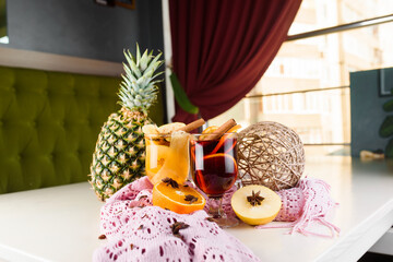Mulled wine, grog and punch hot alcohol drinks on the table with seasonal decoration: pineapple, cinnamon, apple, orange, star anise. Seasonal spiced drink.