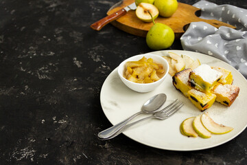 Sliced pie on a white plate with pear jam on a black table. Green pears in the background are blurred. Morning breakfast