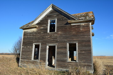 Old abandoned house with rusted roof and broken windows in winter field