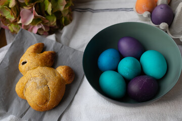 Easter eggs in a bowl in blue, turquoise, purple, and orange, and sweet roll shaped like an easter bunny.