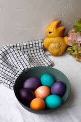 Easter eggs in a bowl in blue, turquoise, purple, and orange, and sweet roll shaped like an easter bunny.
