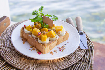 Bread peanut butter in white plate put banana and mango decorated with mint leaves.